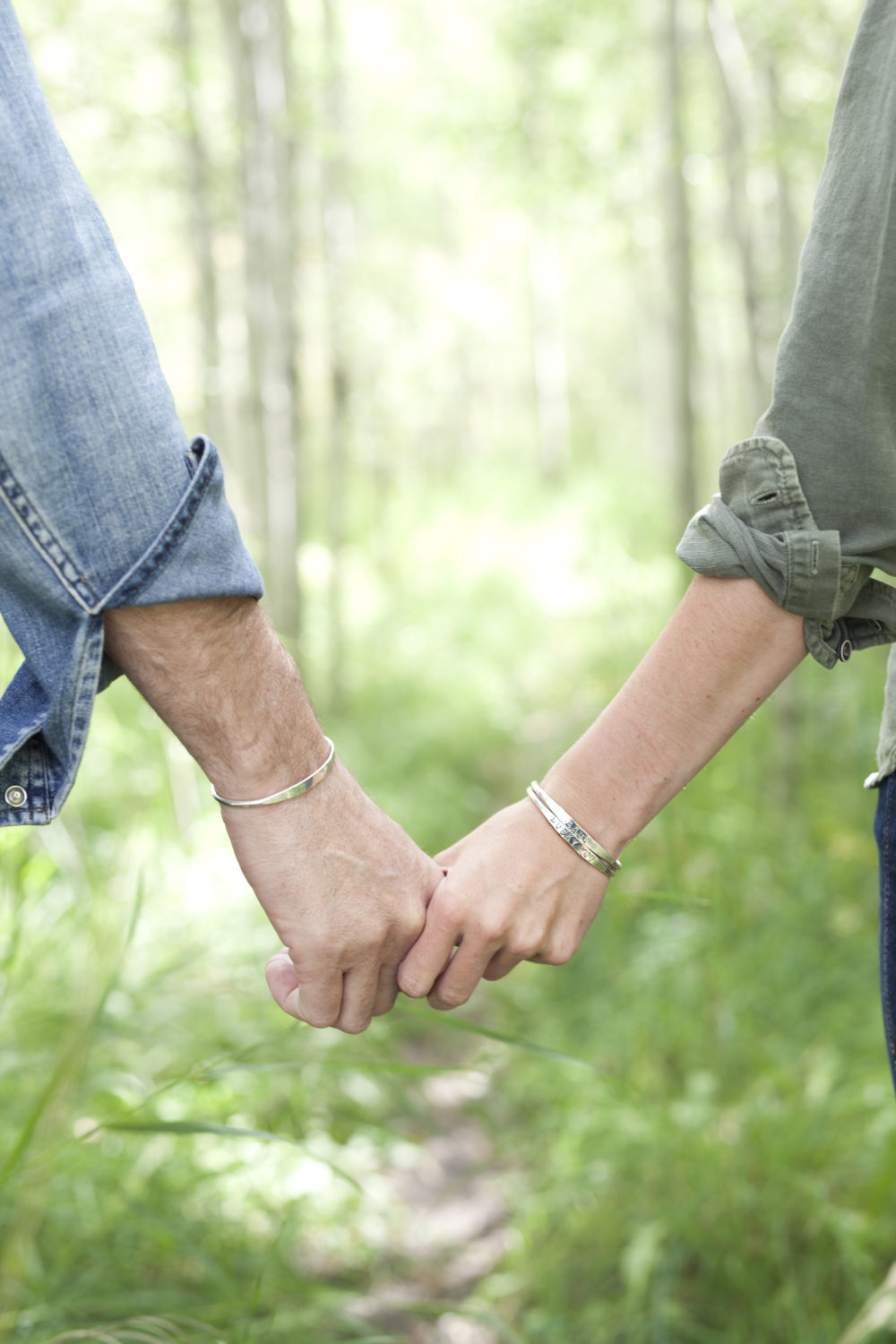 A close up on a man and woman holding hands, each of them wearing the custom stamped bracelets.