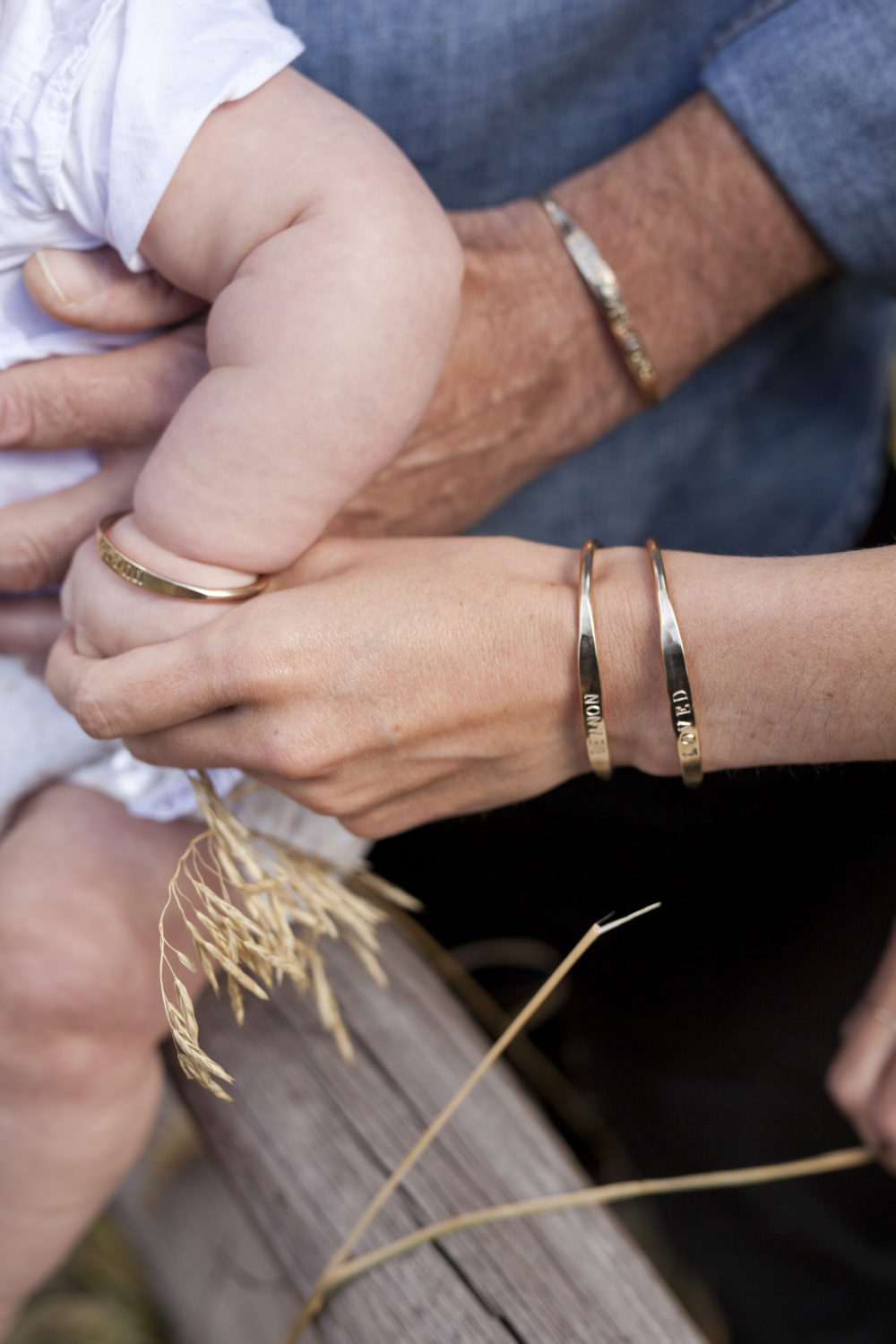 A close up on a father, mother and baby's arms together all wearing the custom stamped bracelets.