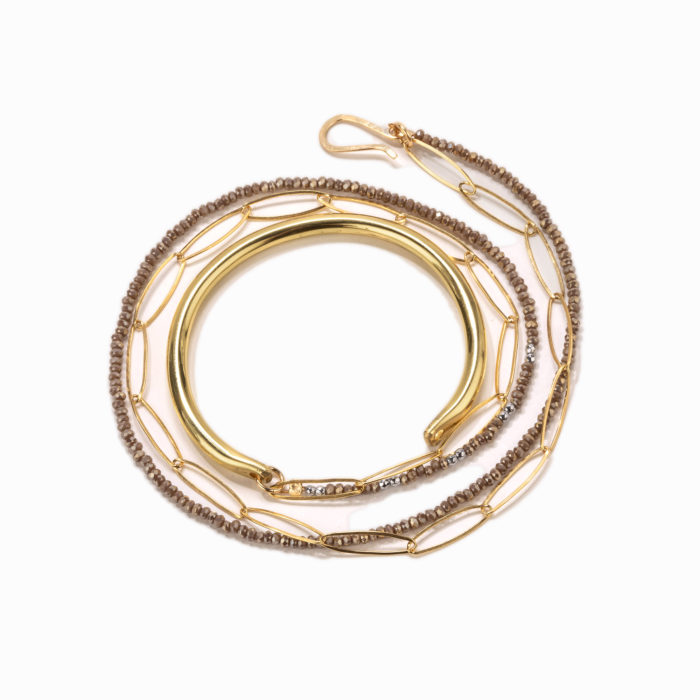 A brass cuff with double wrapped beaded chains in gold and taupe laying in a spiral on a white background.