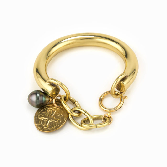 Front view of a chunky brass bracelet with stamped coin charm and tahitian pearl.