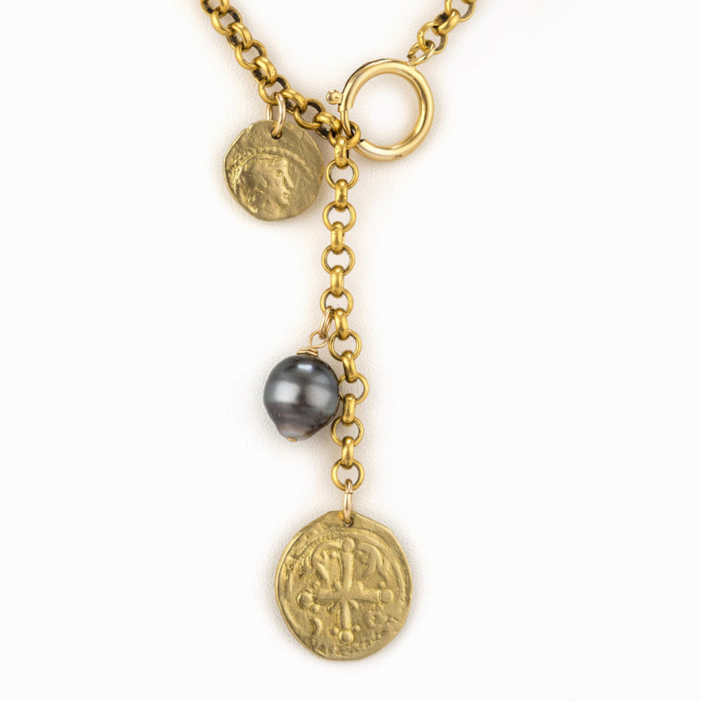 Close up on a a Tahitian pearl and hand casted antique coins hanging from a brass rolo chain.