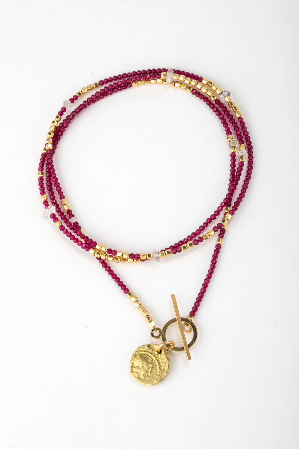 Close up on a tightly wrapped multi garnet and gold African beaded chain necklace with adjustable 14k gold fill closure and antique coin.
