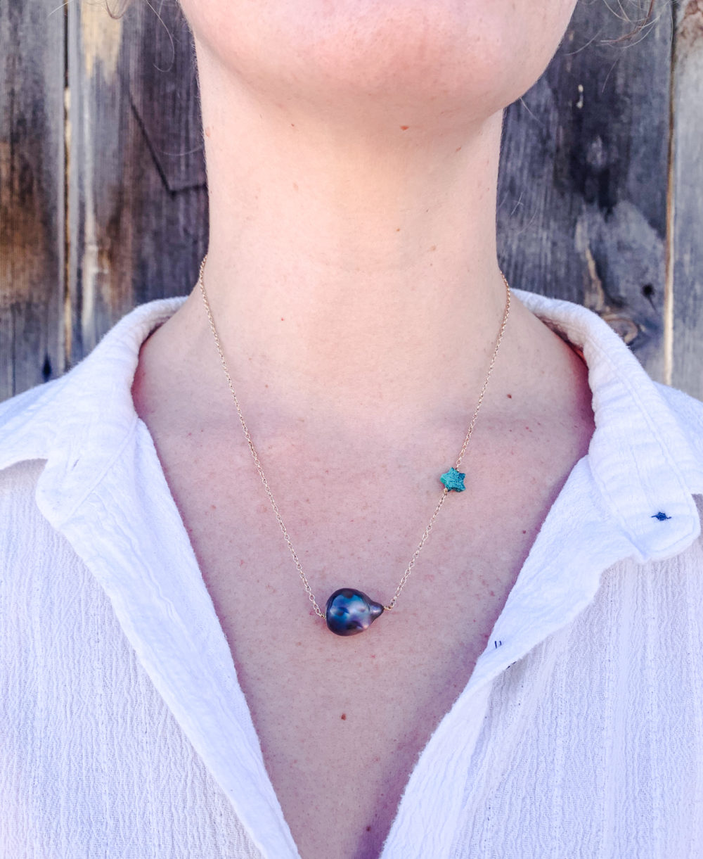 Close up on a woman's neck wearing a 14k gold fill chain necklace with a turquoise star and a black pearl.