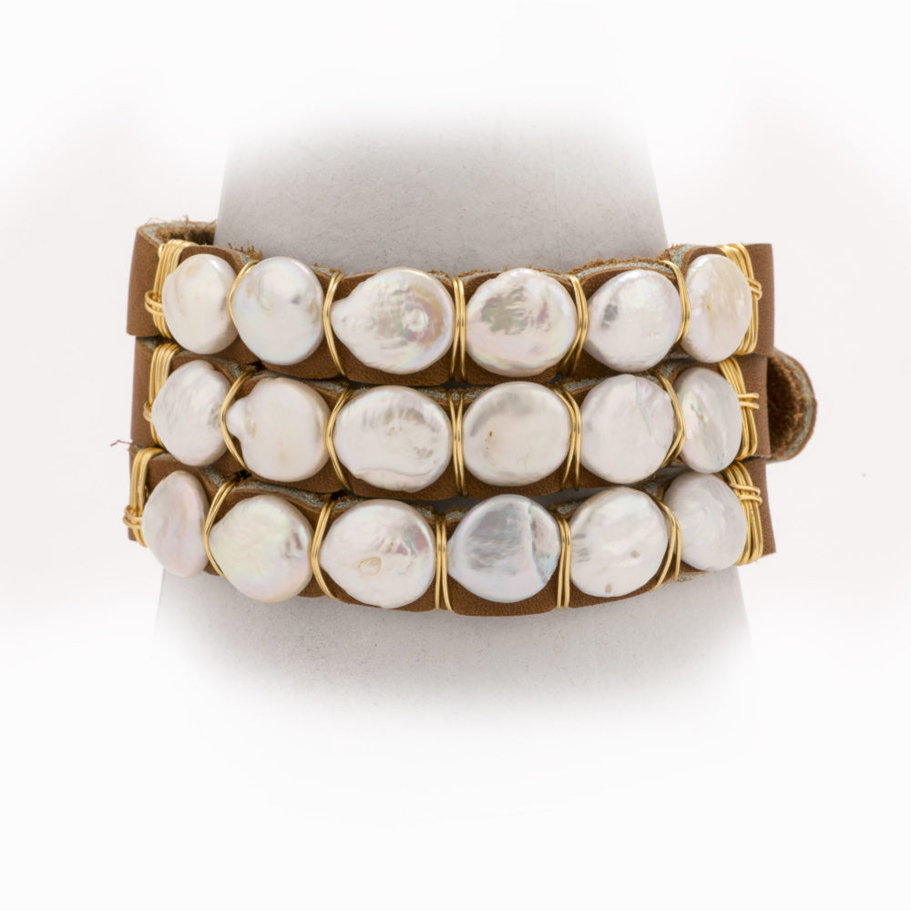Front view of an adjustable tan leather bracelet with 14k gold wire wrapped freshwater pearls resting on a bracelet stand.