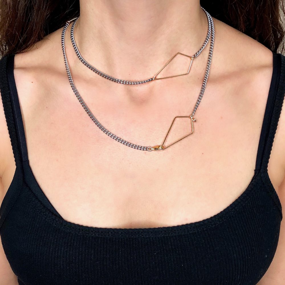 Close up on a woman's torso wearing a simple and delicate necklace with a flat oxidized sterling silver chain with 14K gold-filled diamond geometric detail.