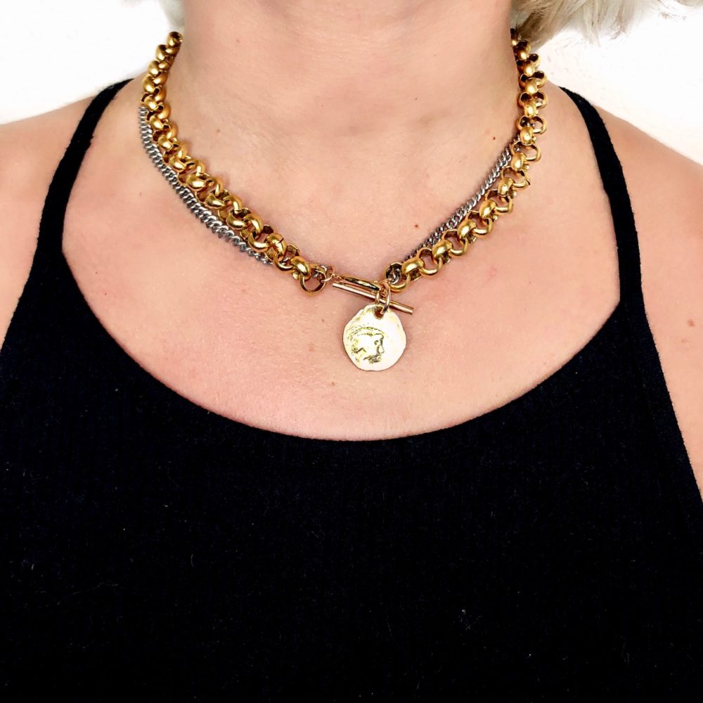 Close up on a woman's torso wearing a flat oxidized sterling silver chain and brass rolo chain necklace with a 14k gold-filled front closure and brass antique coin charm.