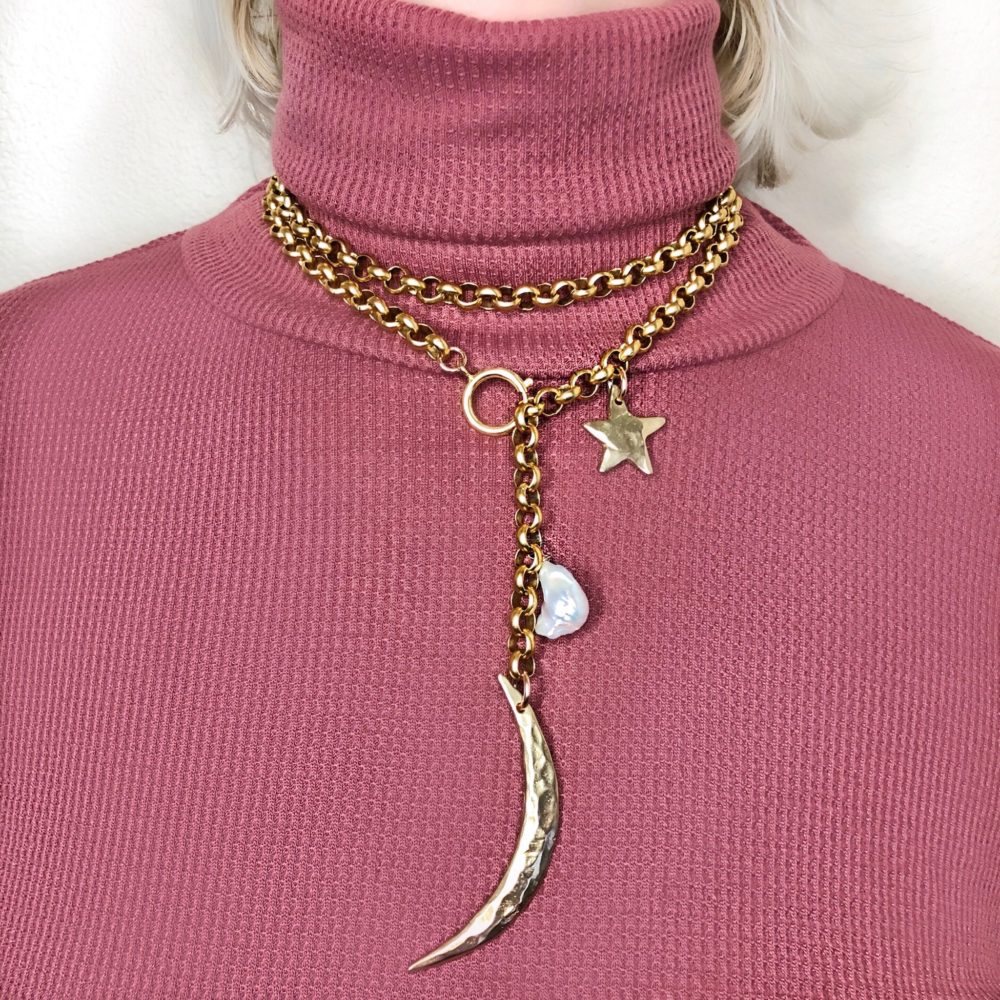 A solid brass rolo chain necklace with an oversized clasp and finshed with a brass moon, star and white pearl.