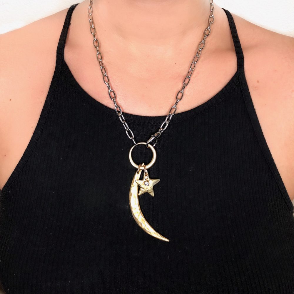 Close up on a woman's neck wearing a black tank top and a large silver chain necklace with adjustable front hook, a solid brass ring and completed with a brass star and moon charm.