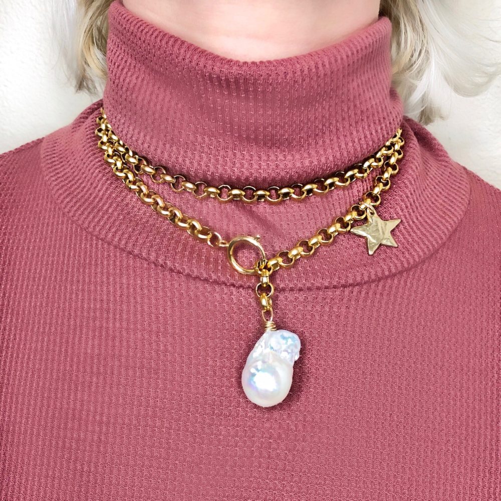 Close up on a woman's torso wearing a large brass chain necklace with large baroque pearl and brass star.