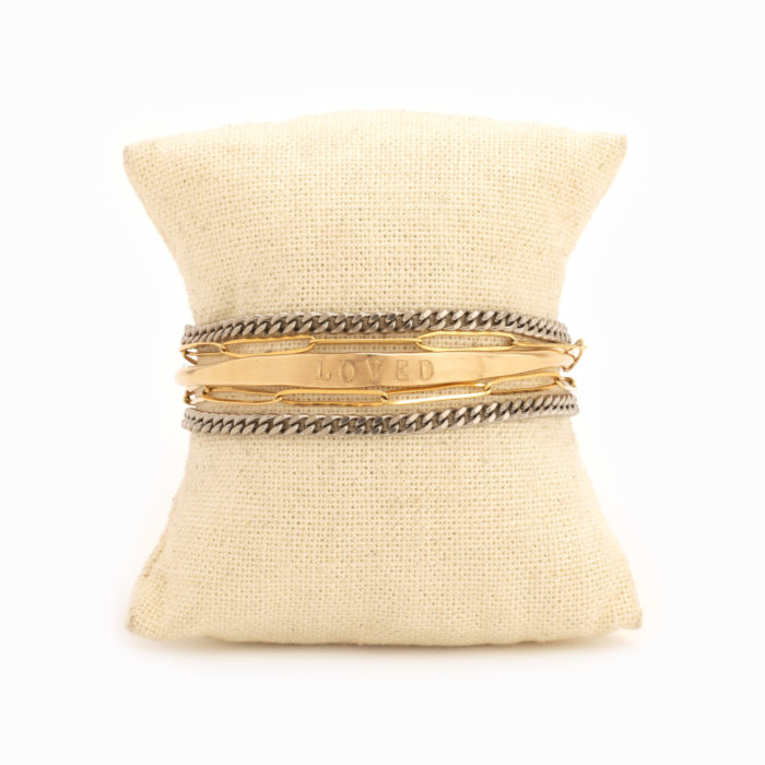 A wire wrap bracelet with oxidized sterling silver chain and 14k gold fill paperclip chain wrap as well as ‘loved’ stamped 14k gold fill bar with added antique coin detail wrapped around a small pillow.