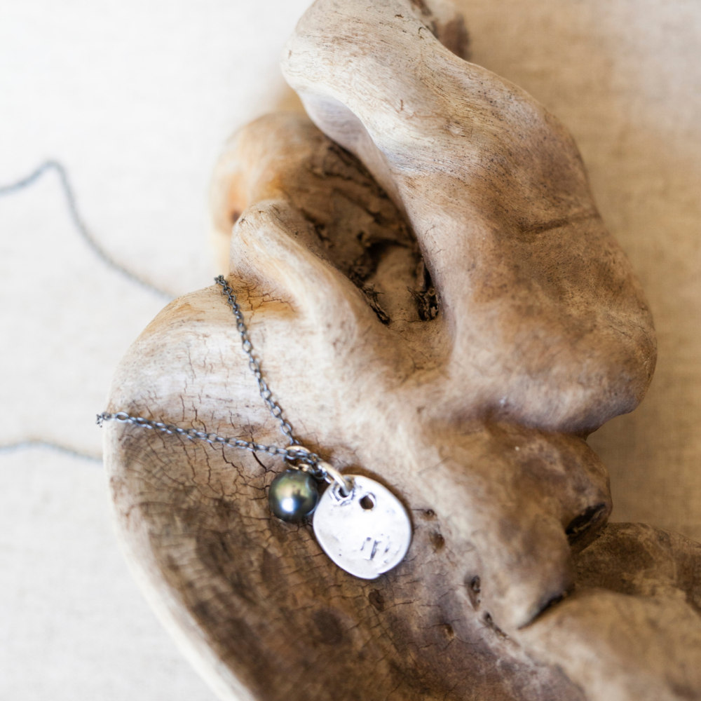 A short necklace with a sterling silver chain and large tahitian pearl laying across a piece of petrified wood.