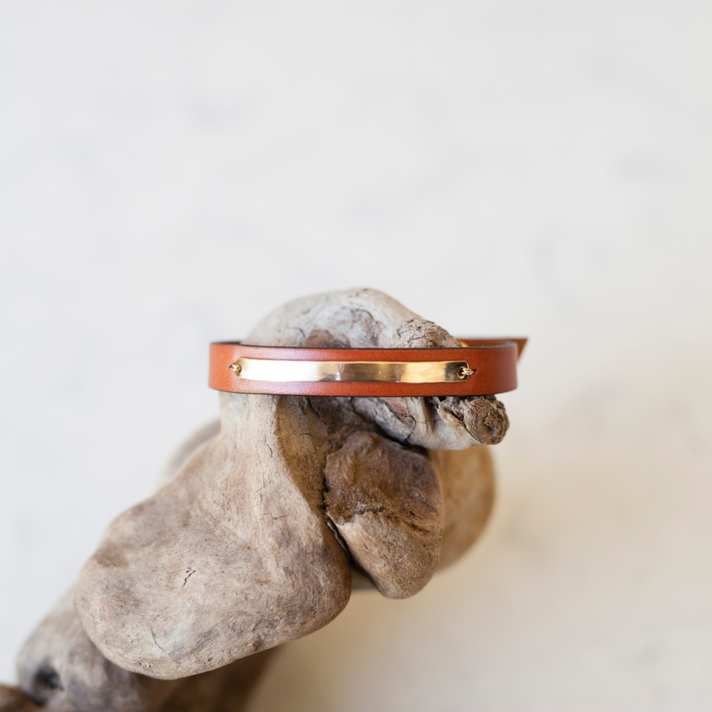Close up on a man's wrist wearing a simple tan leather bracelet with 14k gold filled bar inlay.