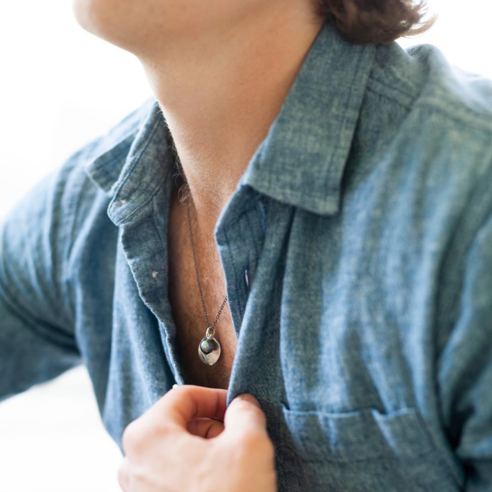 Close up of a man wearing a short necklace with a sterling silver chain and large tahitian pearl.